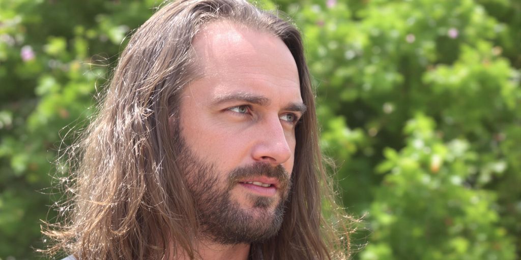 Man with long hair, receding hairline, sunlight.