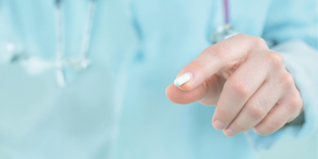Man's hand holding a single finasteride pill